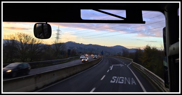 Photo while sat on the coach taken looking through the windscreen overlooking the mountains with Siena written on the road