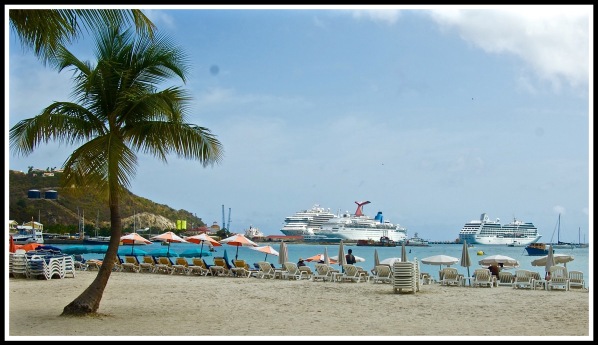 Photo of the beach, with a palm tree on the left, and 2 cruise ships on the right