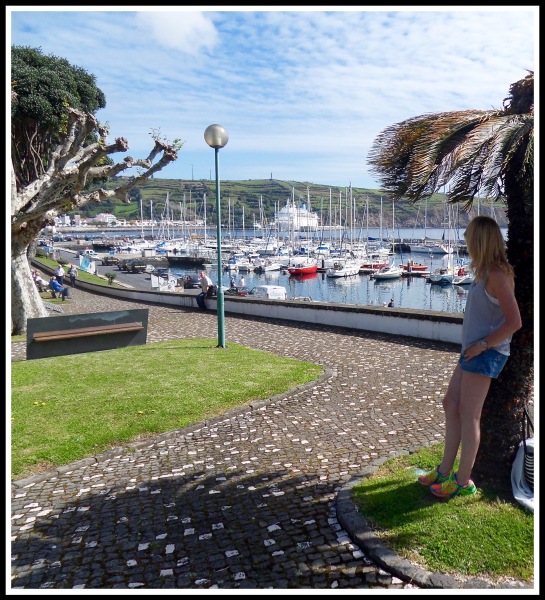 Sarah leaning on a palm tree on the right with the Horta marina and bay filling the rest of the image