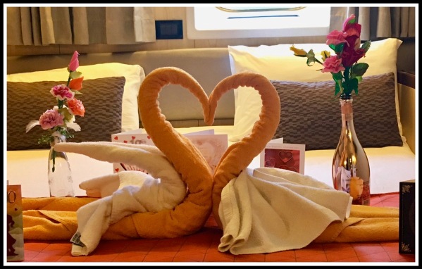 two towel swans together in a love heart shape surrounded by our anniversary cards, on the bed of our cabin on the ship