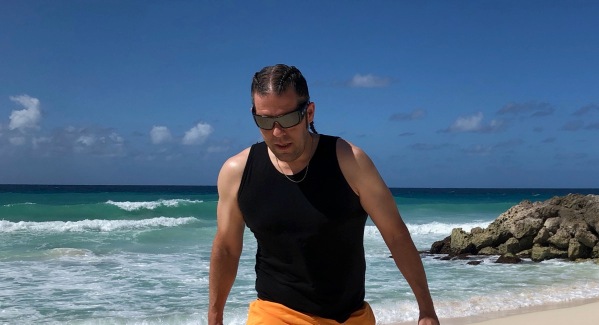 Me wearing a black best and orane shorts waling along the beach in Barbados with braided hair too