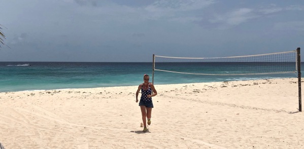 Sarah running towards the camera with a volley ball net on the right on the Barbados beach. The sea is behind her