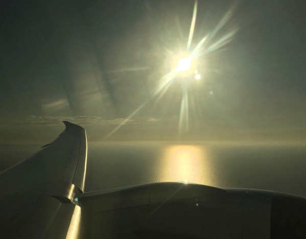 view from the plane window in med flight with the wind on the lower left and the sun spiking down from the top and creating glorious light